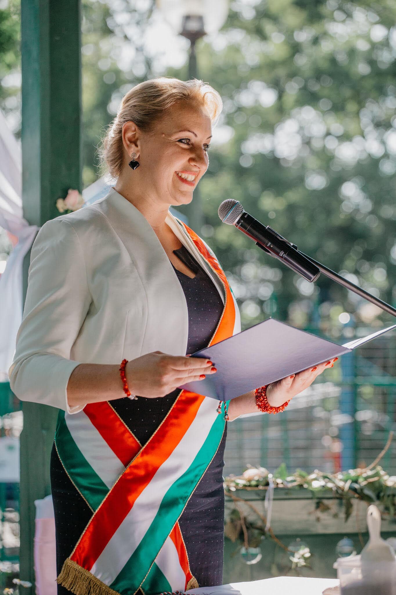 Benkő Angéla esküvői szertartást vezet, mosolyogva a mikrofon előtt